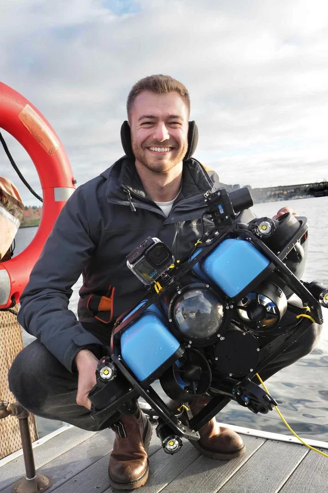 Phil Parisi kneeling on a dock holding the BlueROV2