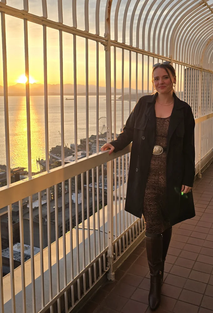 Libbie Barnes standing at an observation deck railing overlooking Elliott Bay at sunset